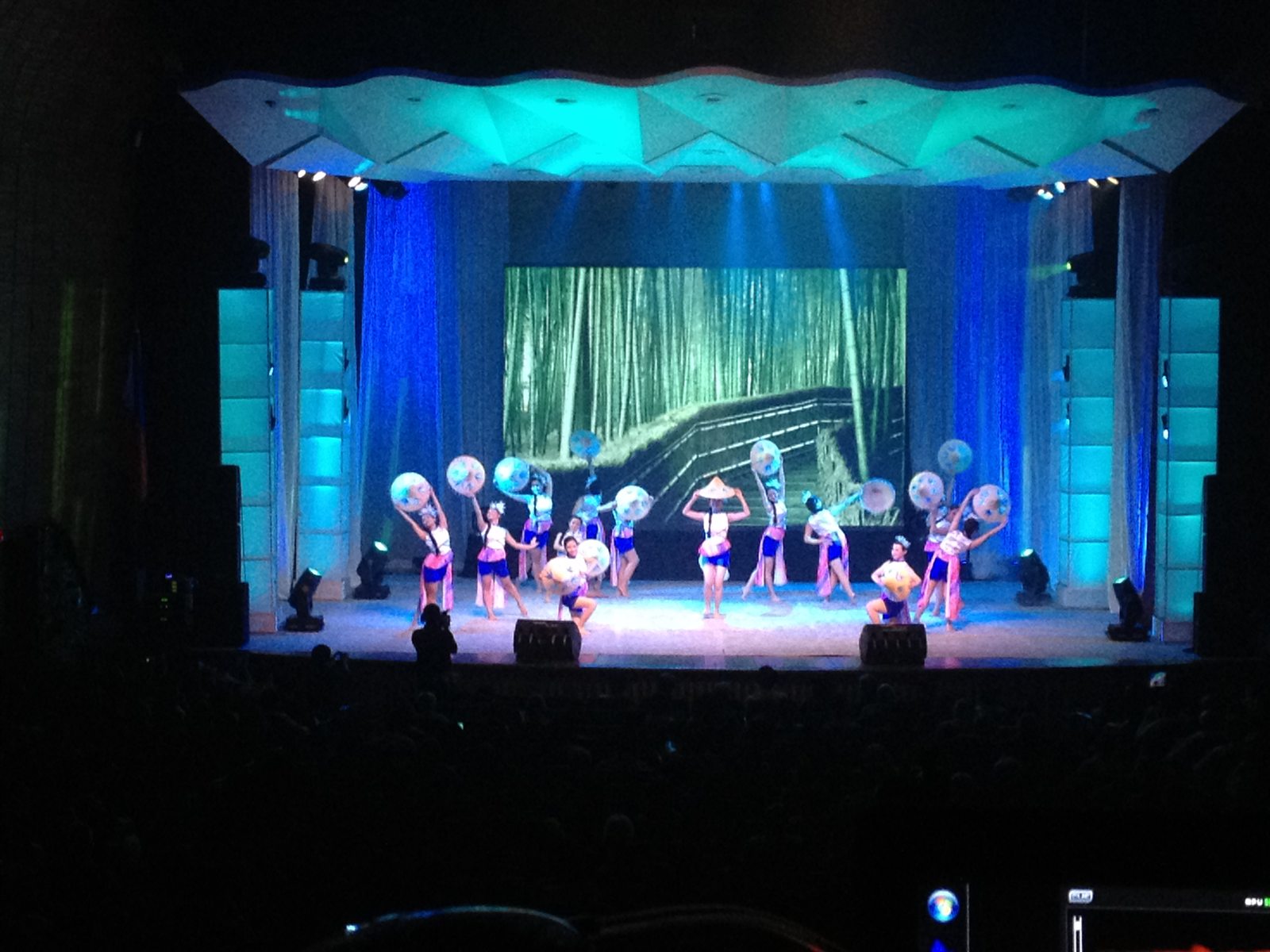 Stage performance set against an illuminated forest projection and cool blue wash